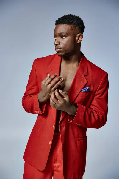 Attractive young african american man in stylish red suit posing on gray backdrop, fashion concept — Stock Photo