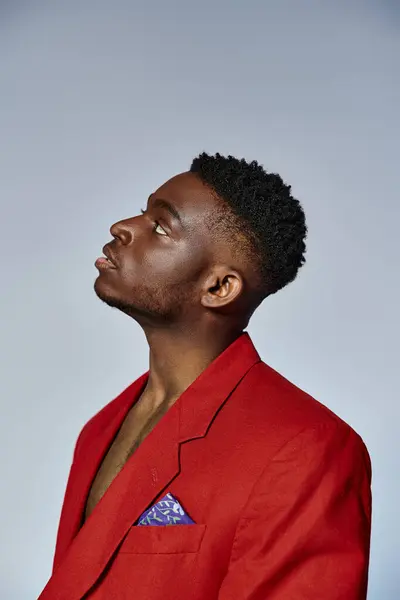 Hombre afroamericano de moda de buen aspecto en traje rojo posando sobre fondo gris, concepto de moda - foto de stock