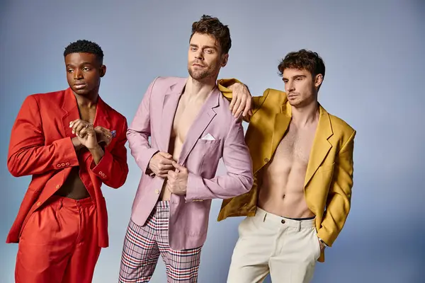 Alluring sexy diverse men in unbuttoned vibrant suits posing on gray backdrop, fashion concept — Stock Photo
