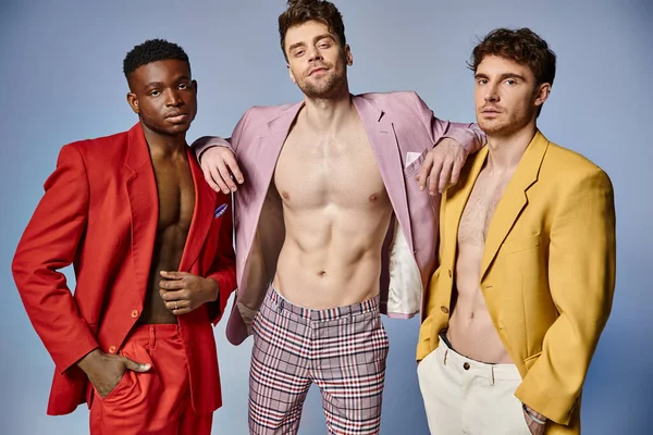 Good looking sexy diverse men in unbuttoned vibrant suits posing on gray backdrop, fashion concept — Stock Photo