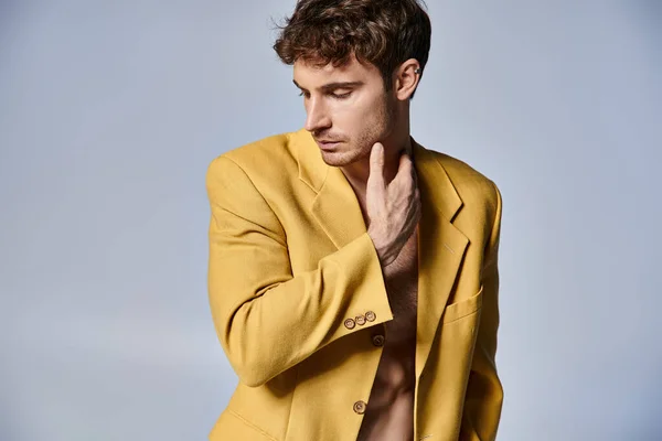 Atractivo joven en elegante chaqueta amarilla posando atractivamente sobre fondo gris, concepto de moda - foto de stock