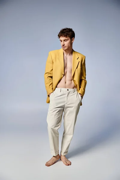 Привлекательный стильный мужчина в желтой куртке привлекательно позирует на сером фоне, концепция моды — стоковое фото