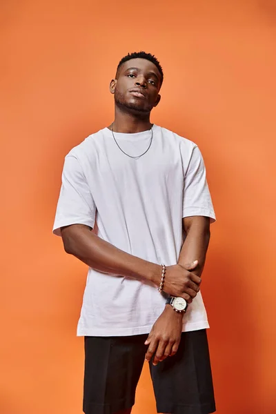 Atraente jovem afro-americano homem na rua roupa casual em pano de fundo laranja, conceito de moda — Fotografia de Stock