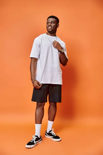 Веселий молодий афроамериканський чоловік на вуличному повсякденному вбранні на помаранчевому тлі, концепція моди — стокове фото