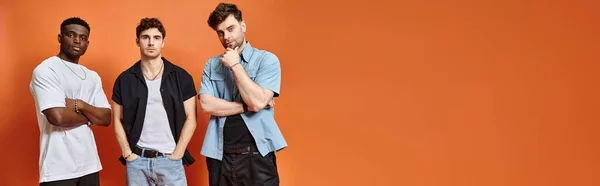 Handsome multicultural friends in casual urban outfits posing together on orange backdrop, banner — Stock Photo