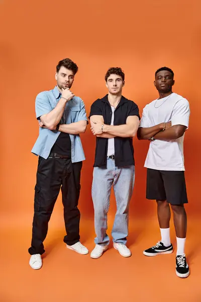Three handsome multiracial friends in casual urban outfits posing together on orange backdrop — Stock Photo