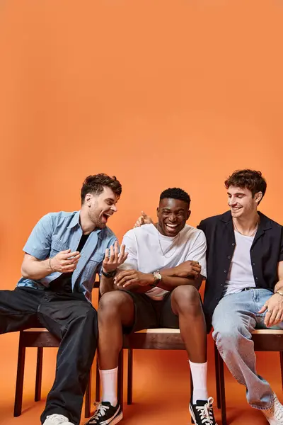 Joyous diverse men in casual street outfits smiling happily on orange backdrop, fashion concept — Stock Photo