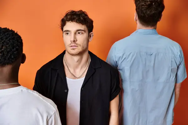 Focus on handsome man in urban attire looking at camera with back view of his diverse friends — Stock Photo