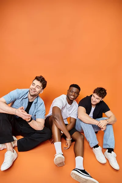 Handsome cheerful friends in urban everyday clothes sitting on floor and smiling joyfully, fashion — Stock Photo