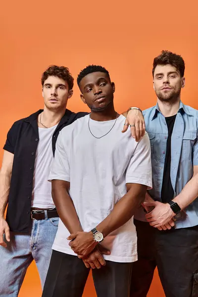Appealing fashionable diverse friends in urban attires posing on orange backdrop, fashion concept — Stock Photo
