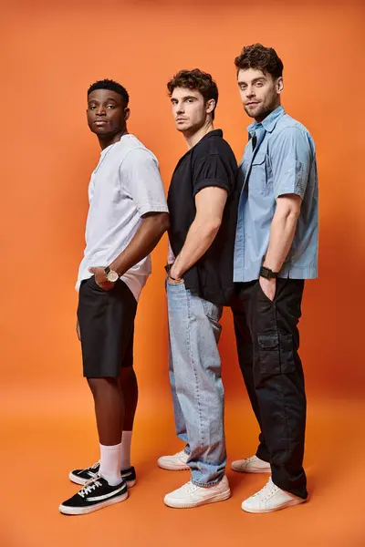 Attraktive, elegante Freunde in urbaner Kleidung posieren vor orangefarbenem Hintergrund, Modekonzept — Stockfoto