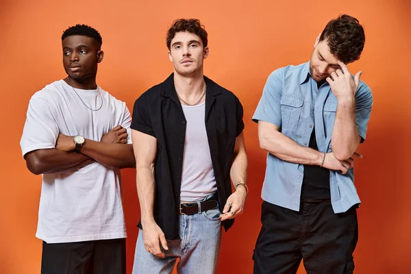 Appealing multiracial male models in stylish urban clothes posing on orange backdrop, fashion — Stock Photo