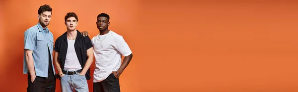 Handsome diverse men in trendy urban clothes posing on orange backdrop, fashion concept, banner — Stock Photo