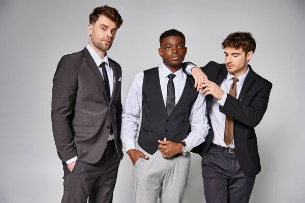 Attractive young multicultural friends in smart business suits posing together on gray backdrop — Stock Photo