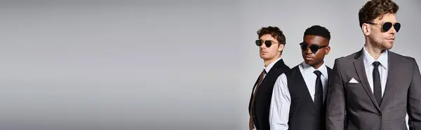 Bellissimo uomo diversificato in eleganti abiti eleganti con occhiali da sole in posa su sfondo grigio, banner — Foto stock