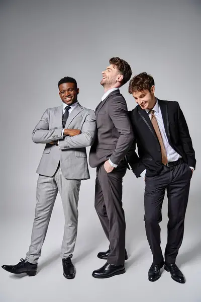 Happy multiracial friends in business casual outfits posing on gray backdrop and smiling joyfully — Stock Photo