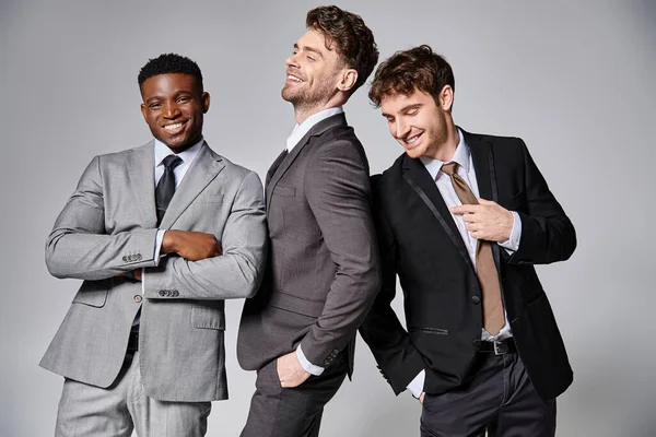Happy multicultural friends in business casual outfits posing on gray backdrop and smiling joyfully — Stock Photo