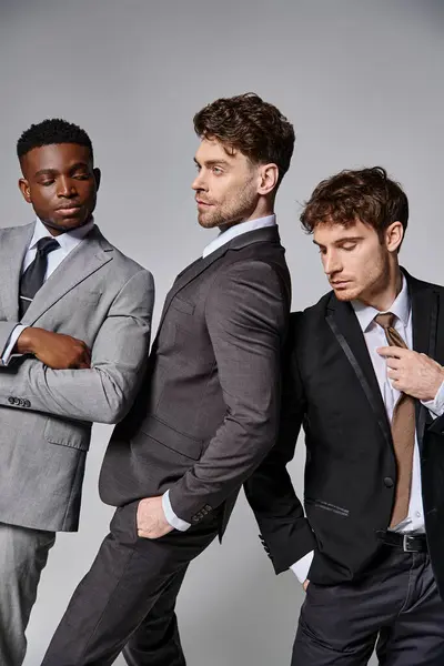 Young attractive multicultural men in business smart suits posing together on gray background — Stock Photo