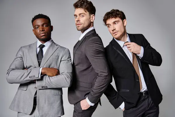 Giovani uomini multiculturali belli in abiti business smart in posa insieme su sfondo grigio — Foto stock