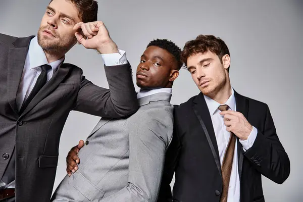 Jeunes beaux hommes multiculturels en affaires costumes intelligents posant ensemble sur fond gris — Photo de stock