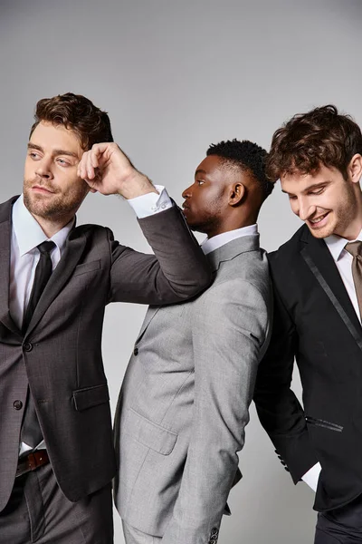 Jolly multicultural men in business casual outfits posing on gray backdrop and smiling cheerfully — Stock Photo