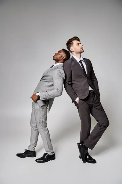 Deux modèles masculins multiculturels attrayants et élégants dans des vêtements intelligents d'affaires posant sur fond gris — Photo de stock
