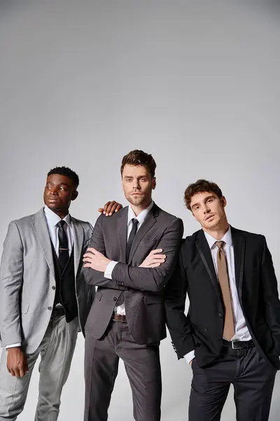 Attrayants jeunes modèles masculins multiculturels en tenue décontractée d'affaires posant sur fond gris — Photo de stock