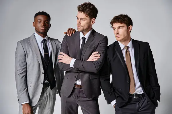 Attractive young interracial friends in smart business suits posing together on gray background — Stock Photo