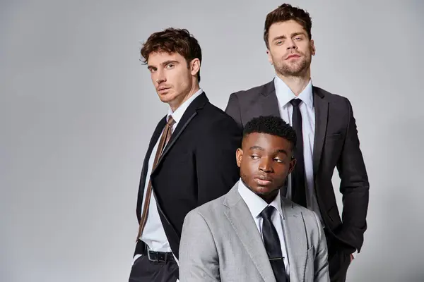 Guapo joven multicultural macho modelos en negocios casual trajes posando en gris telón de fondo - foto de stock
