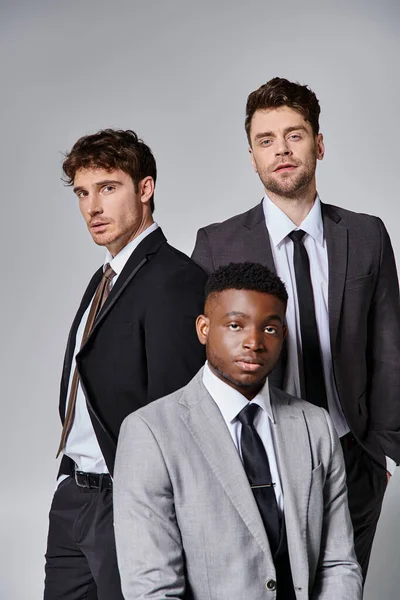 Appealing young diverse friends in smart business suits posing together on gray background — Stock Photo