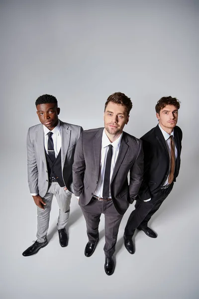 Handsome young multiethnic friends in smart business suits posing together on gray background — Stock Photo