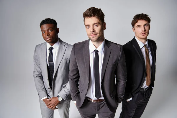 Atractivo jóvenes modelos masculinos multiculturales en trajes casuales de negocios posando sobre fondo gris - foto de stock
