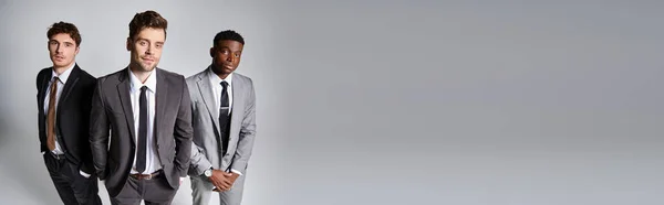 Handsome multiethnic friends in smart business suits posing together on gray background, banner — Stock Photo
