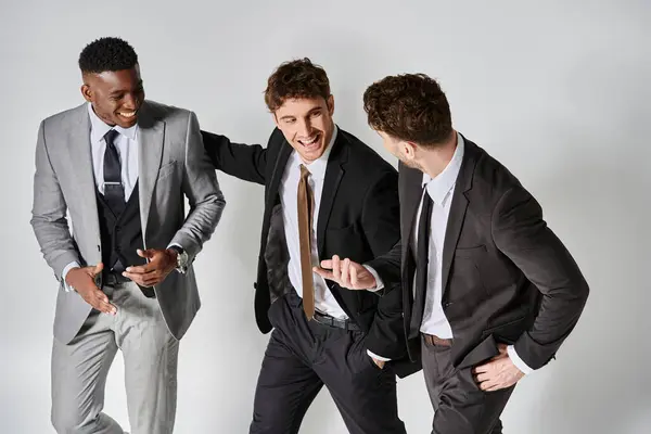 Young happy multicultural friends in business elegant attires smiling joyfully on gray background — Stock Photo