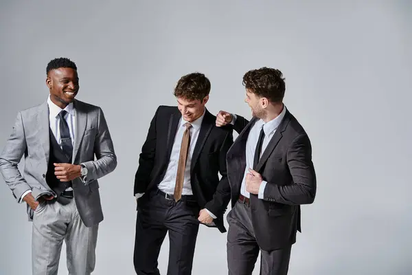 Atrativo alegre diversos amigos em negócios elegantes trajes sorrindo alegremente no fundo cinza — Fotografia de Stock