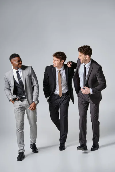 Good looking happy young diverse male models in smart suits smiling sincerely on gray backdrop — Stock Photo