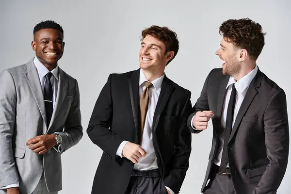 Good looking cheerful diverse male models in smart suits smiling sincerely on gray backdrop — Stock Photo