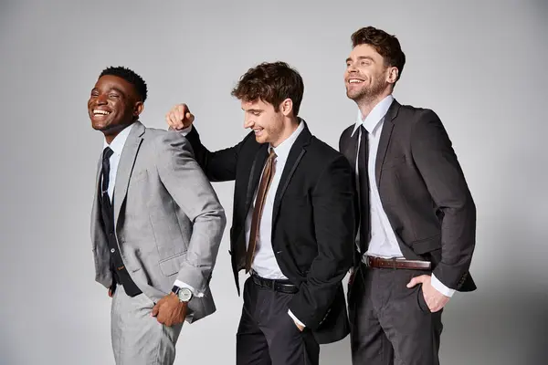 Appealing happy multicultural male models in smart suits smiling sincerely on gray backdrop — Stock Photo