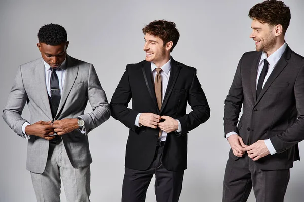 Attrayants modèles masculins multiculturels joyeux en costumes intelligents souriant sincèrement sur fond gris — Photo de stock