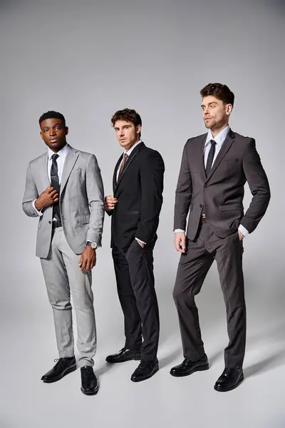 Attractive stylish multicultural male models in business elegant smart suits posing on gray backdrop — Stock Photo