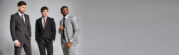 Attraente interrazziale maschio modelli in affari elegante intelligente abiti in posa su sfondo grigio, banner — Foto stock