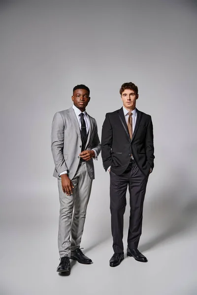 Appealing young multicultural friends in smart suits posing on gray backdrop and looking at camera — Stock Photo
