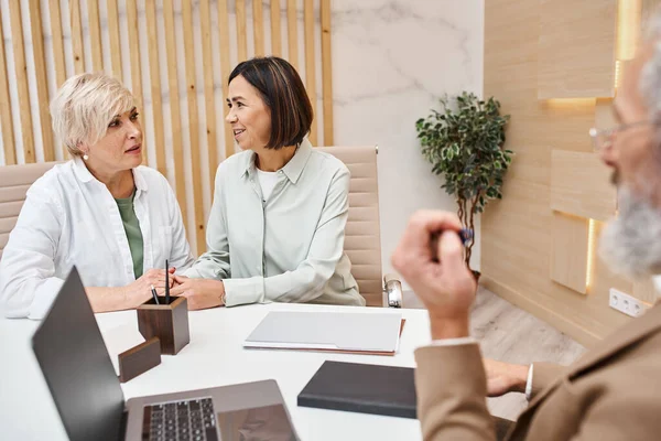 Middle aged multicultural lgbt couple discussing property near bearded realtor in real estate office — Stock Photo