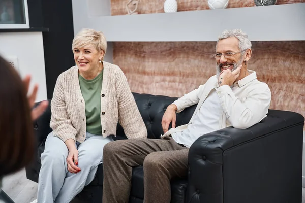 Feliz casal de meia idade sentado no sofá de couro e olhando para o psicólogo durante a consulta — Fotografia de Stock