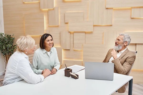 Middle aged interracial lgbt couple discussing property near bearded realtor in real estate office — Stock Photo
