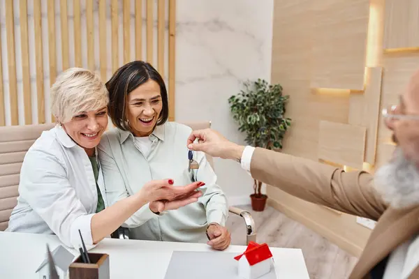 Middle aged realtor giving house key to excited interracial lgbt couple in real estate office — Stock Photo