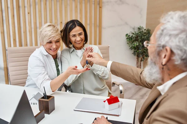 Makler gibt Hausschlüssel an aufgeregtes Paar mittleren Alters in Immobilienbüro — Stockfoto