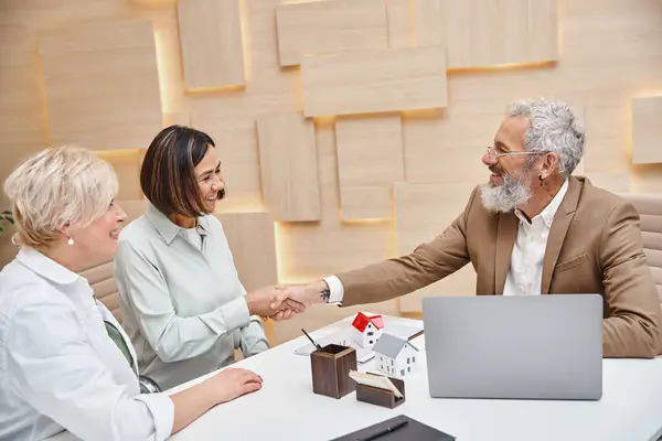 Realtor shaking hand with middle aged multiracial woman near lesbian partner  in real estate office — Stock Photo
