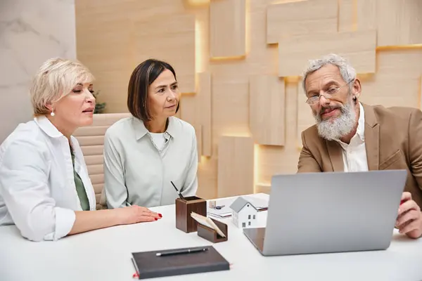 Realtor showing laptop with house projects to middle aged lgbt couple in real estate office — Stock Photo