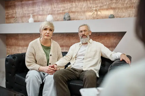 Attentive middle aged couple sitting on leather couch and looking at psychologist during consult — Stock Photo